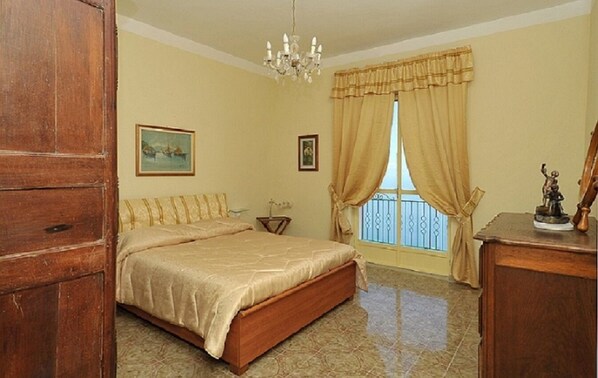 A bedroom with a bed, a chandelier, a window with curtains, and a statue on a dresser. - Apartment with breathtaking view (Furore)