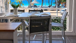 An outdoor dining area with a view of the beach and ocean, a potted plant, and a table set for two. - Beachfront & Town Center • 2 Bedrooms • 2 Ensuite Baths (Le Diamant)