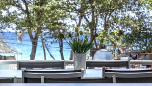 A table with a vase of tulips, a view of the sea, and trees in the background. - Beachfront & Town Center • 2 Bedrooms • 2 Ensuite Baths (Le Diamant)