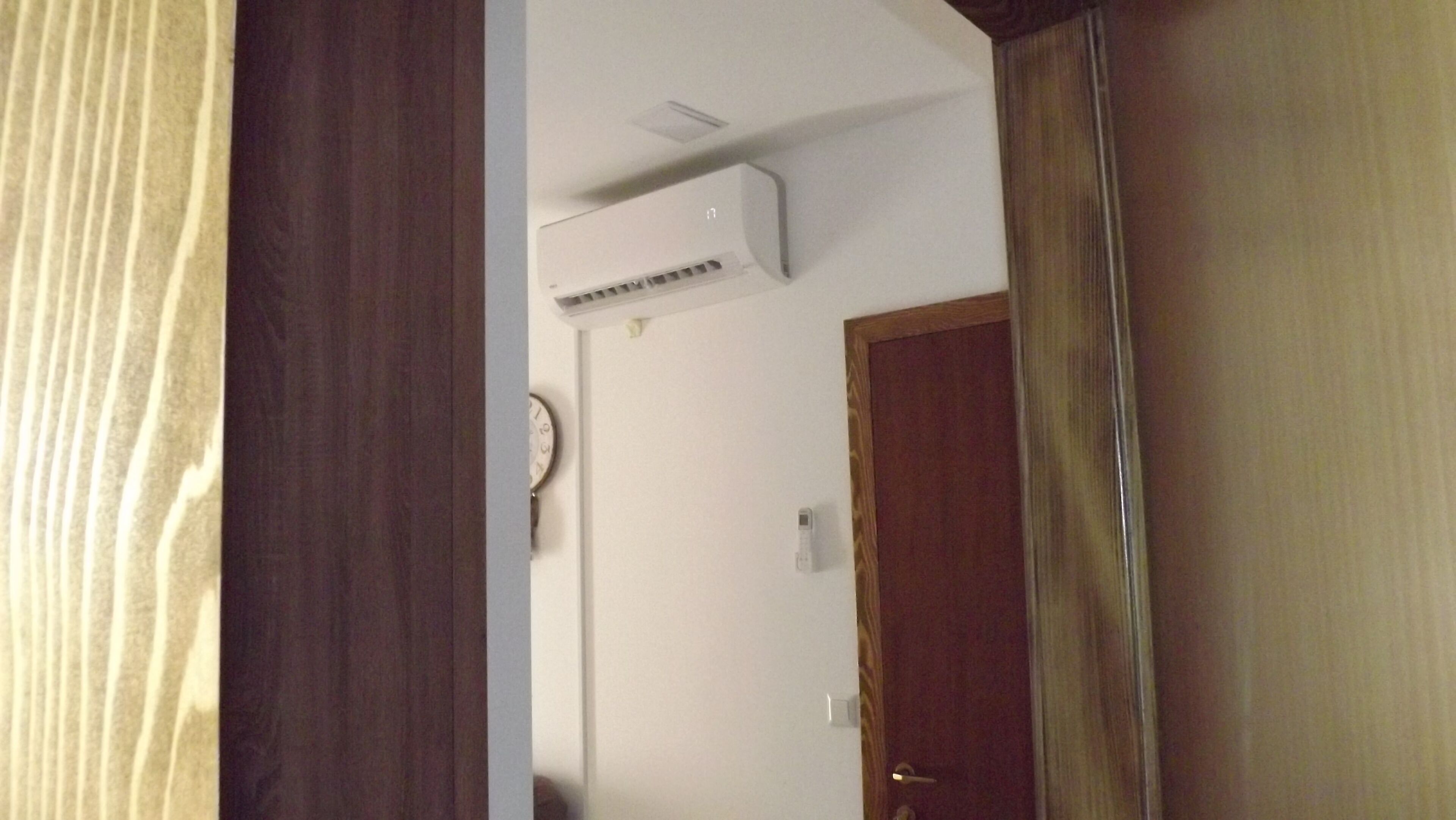 Una habitación con puerta de madera, pared blanca y aire acondicionado instalado en el techo.