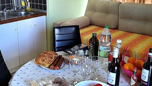Un comedor con una mesa preparada para dos personas, que incluye pan, salchichas, copas de vino y botellas.