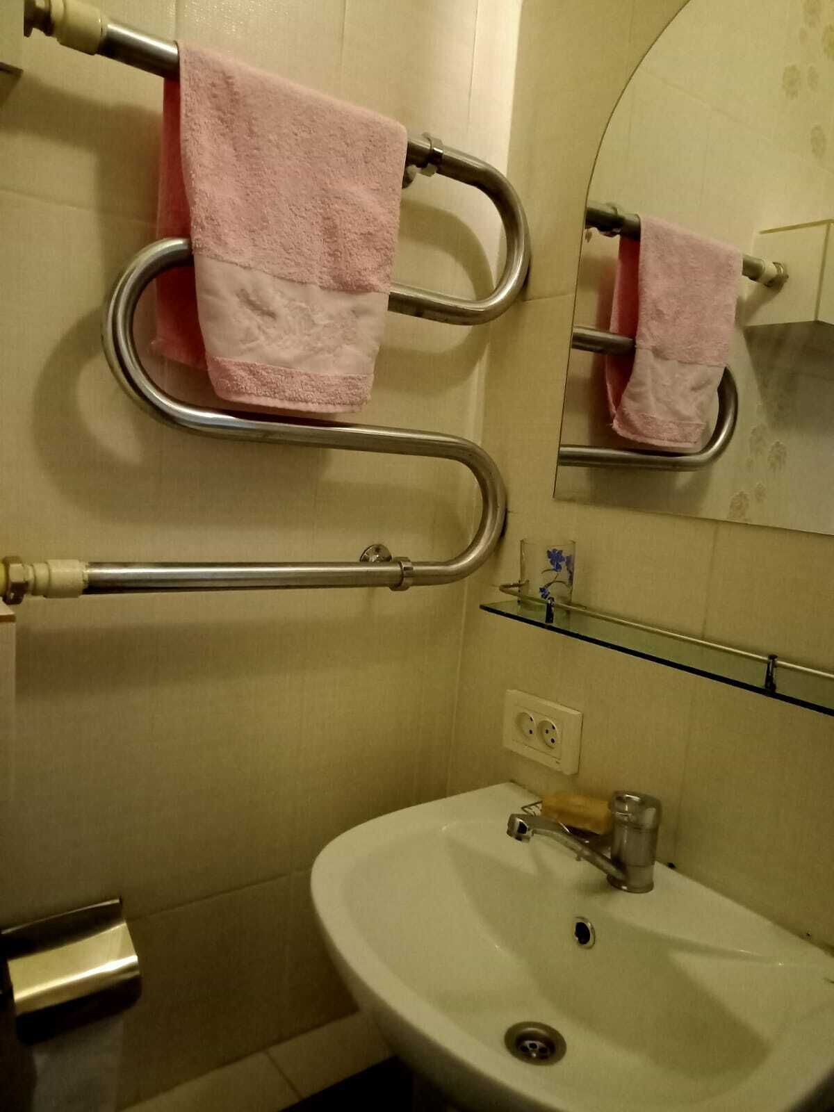 Une salle de bain avec un lavabo blanc, un miroir et deux serviettes roses posées sur des porte-serviettes.