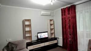 Ein Wohnzimmer mit Fernseher, zwei Regalen, einer Couch und einem roten Vorhang.