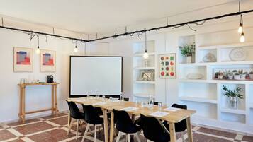 A conference room with a long table, black chairs, a whiteboard, and shelves with plants and decorative items.