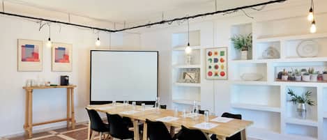 Un salón de conferencias con una larga mesa, sillas negras, una pizarra y estanterías con plantas y objetos decorativos.