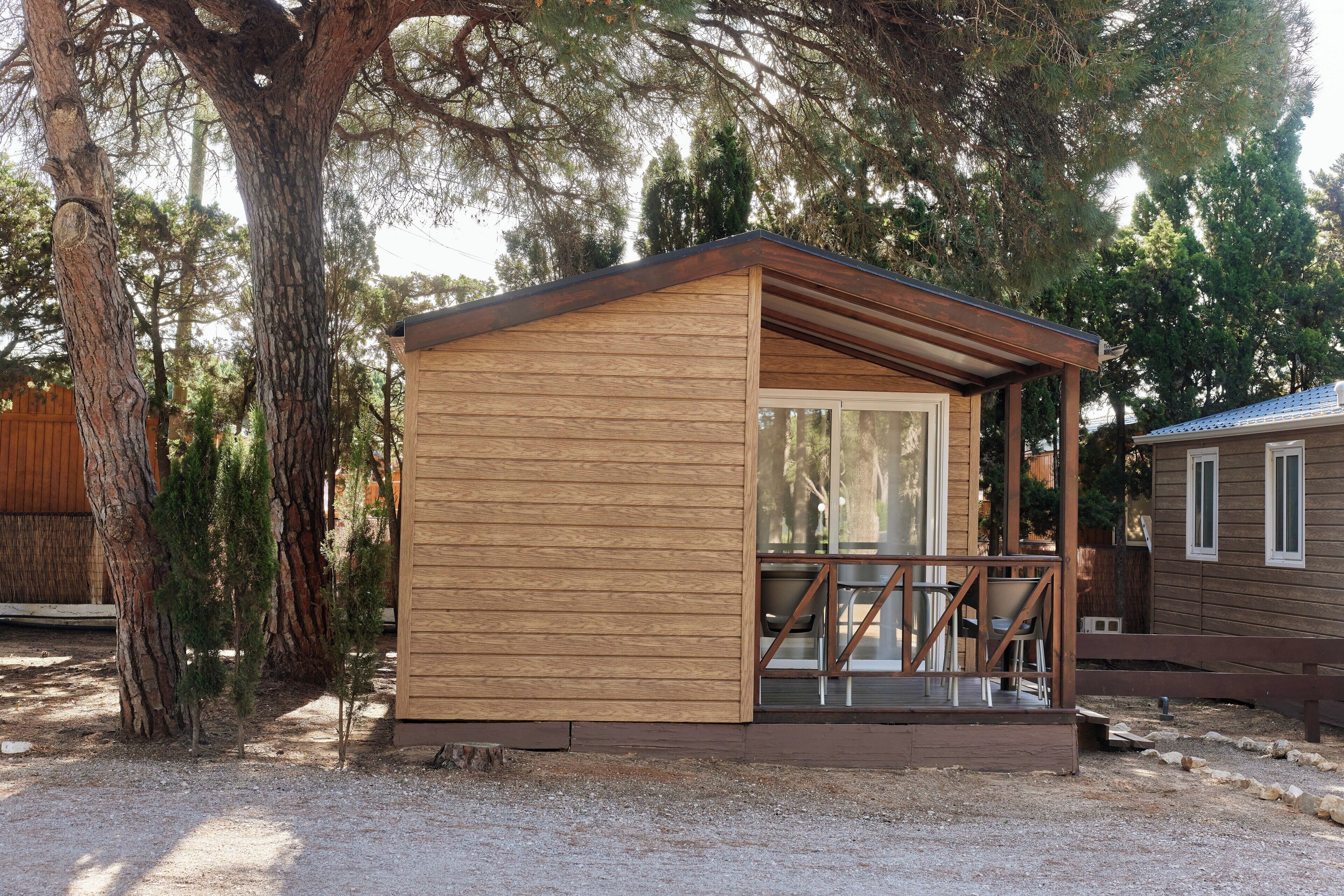 Una pequeña cabaña de madera con un porche y puerta de cristal, rodeada de árboles.