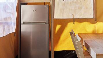 Una cocina compacta con microondas y refrigerador integrados, piso de madera y un banco en la mesa.