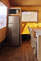 Una cocina compacta con microondas y refrigerador integrados, piso de madera y un banco en la mesa.