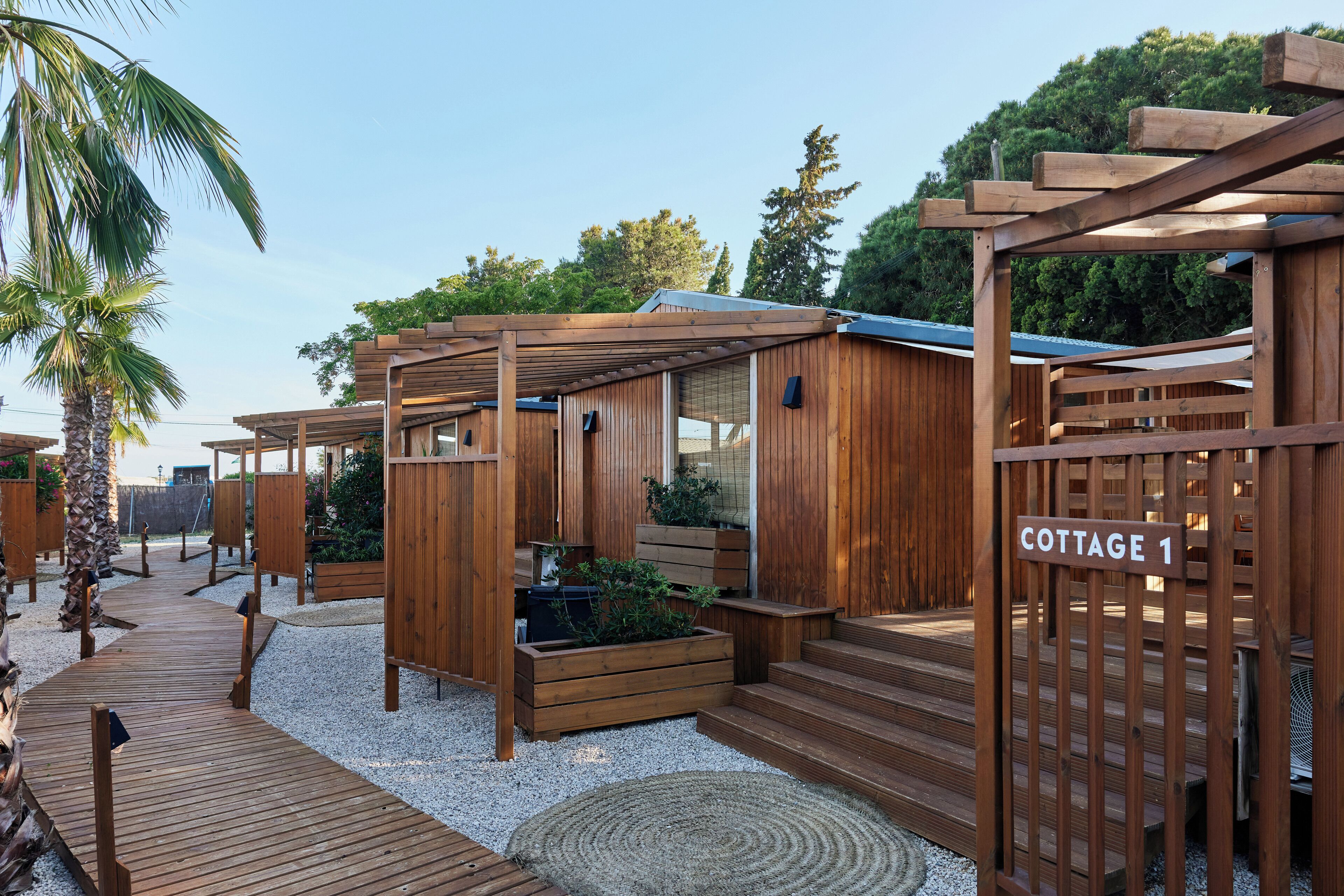 Una cabaña de madera con un porche de madera, un pequeño jardín y un letrero que indica 'COTTAGE 1'.