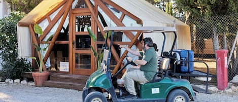 Un hombre conduce un carrito de golf hacia un edificio rústico con estructura de madera y un toldo grande.