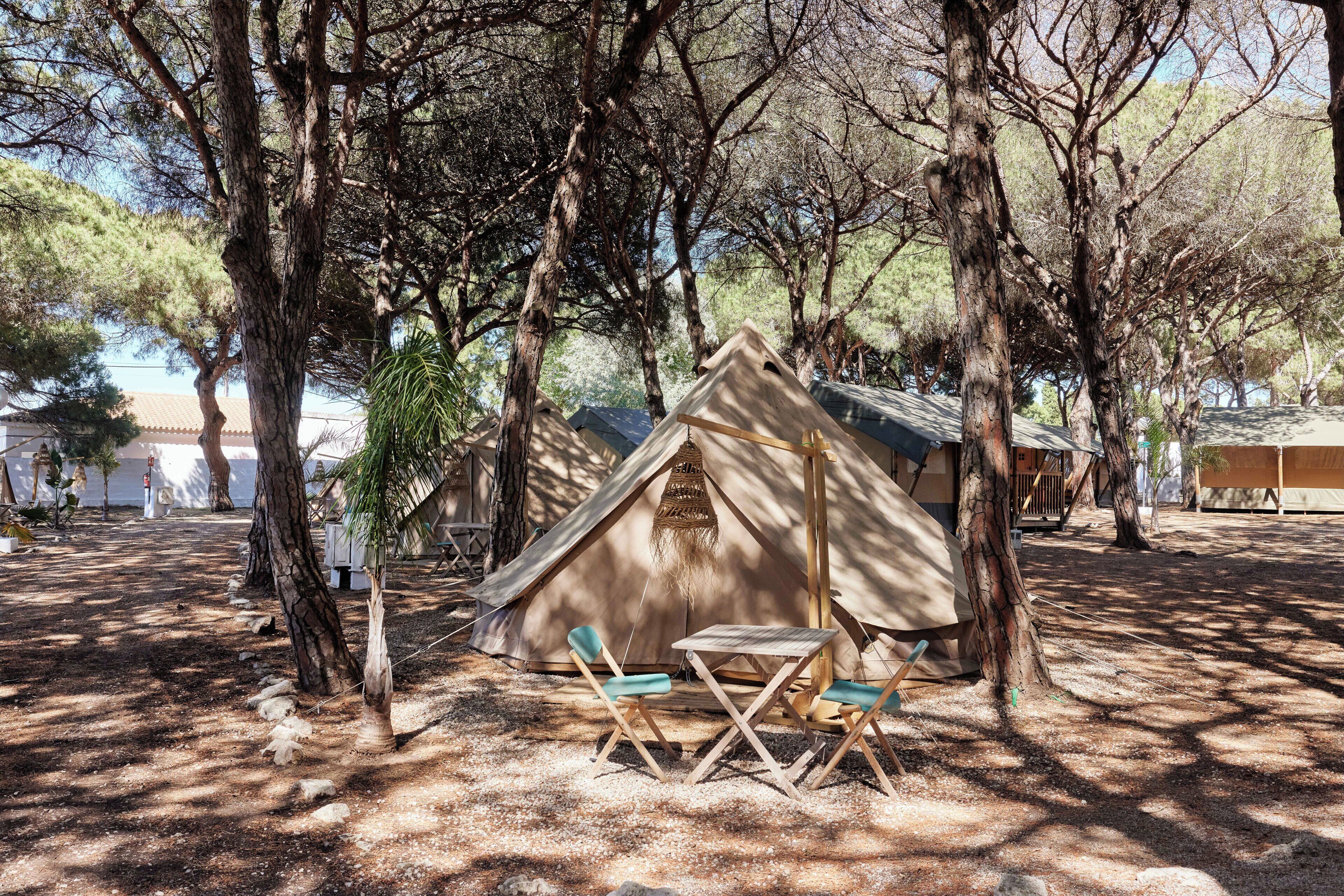 A rustic tent with a table and chairs in a wooded area.