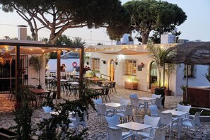 An outdoor patio area with tables and chairs, surrounded by potted plants and trees. - TAIGA Conil (Conil de la Frontera)