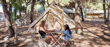 Uma tenda com estrutura de madeira e telhado de palha, cercada por árvores.