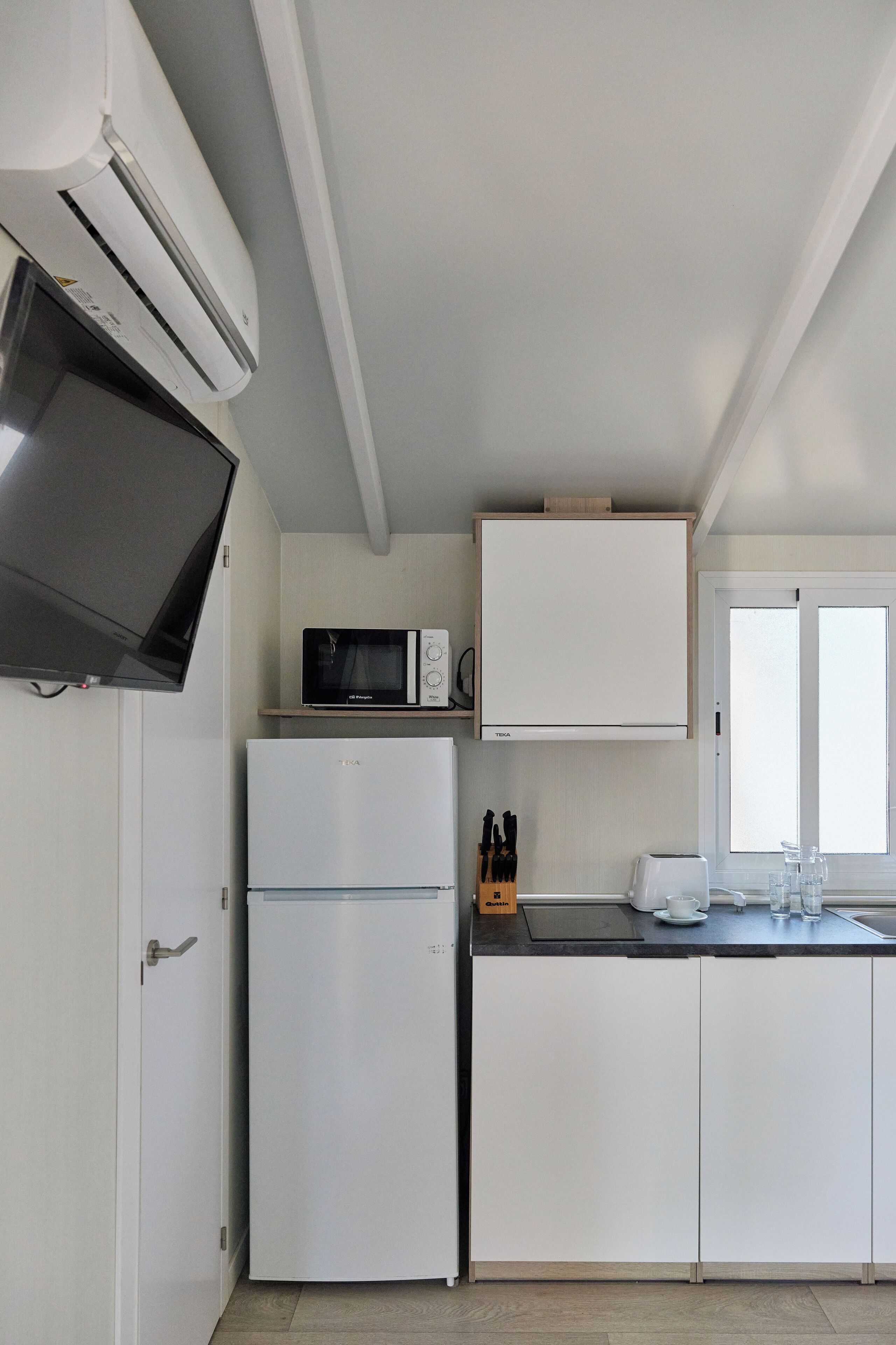 Cocina compacta con refrigerador, microondas y televisor de pantalla plana montado en la pared.