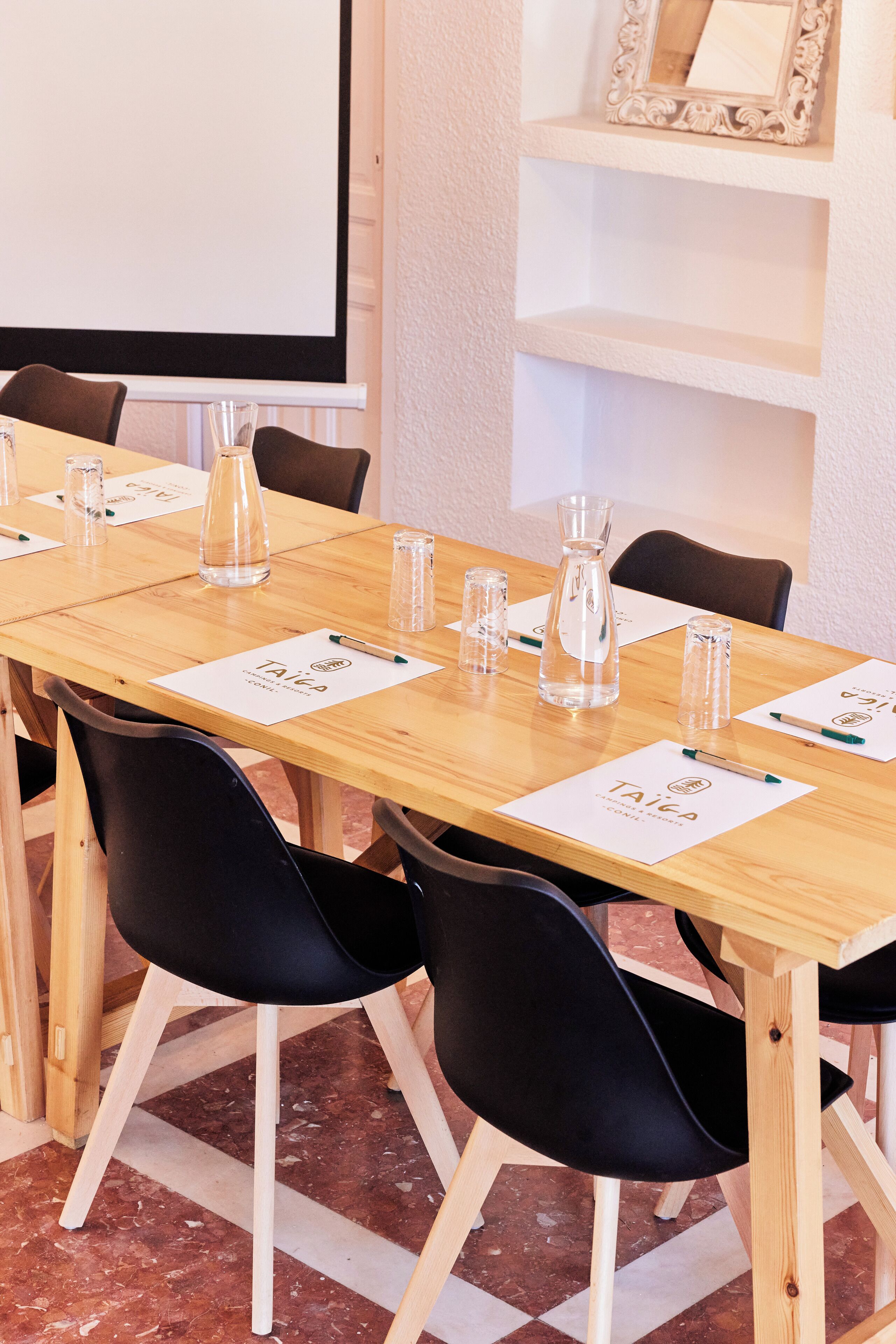 A conference room with a long wooden table, black chairs, and a projector screen.