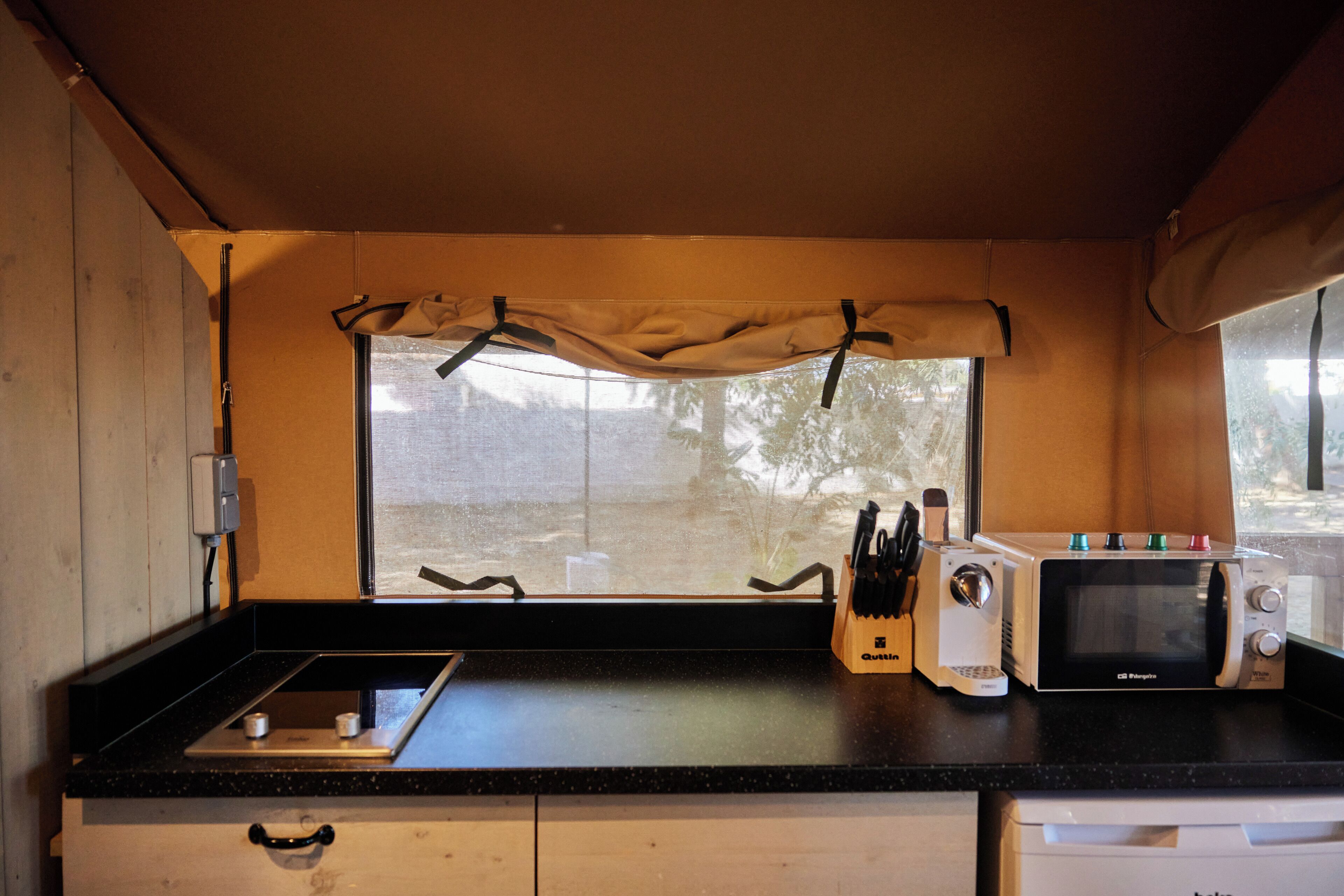 A compact kitchen with a window, a microwave, a toaster, and a knife block.