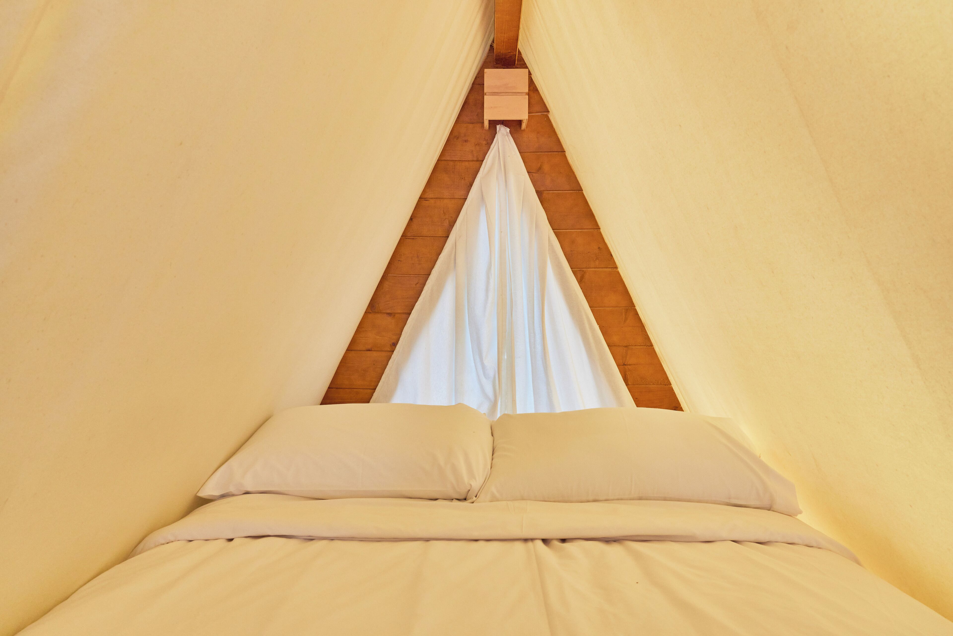 Una cama con ropa de cama blanca y cabecera de madera en una habitación con paredes color beige.