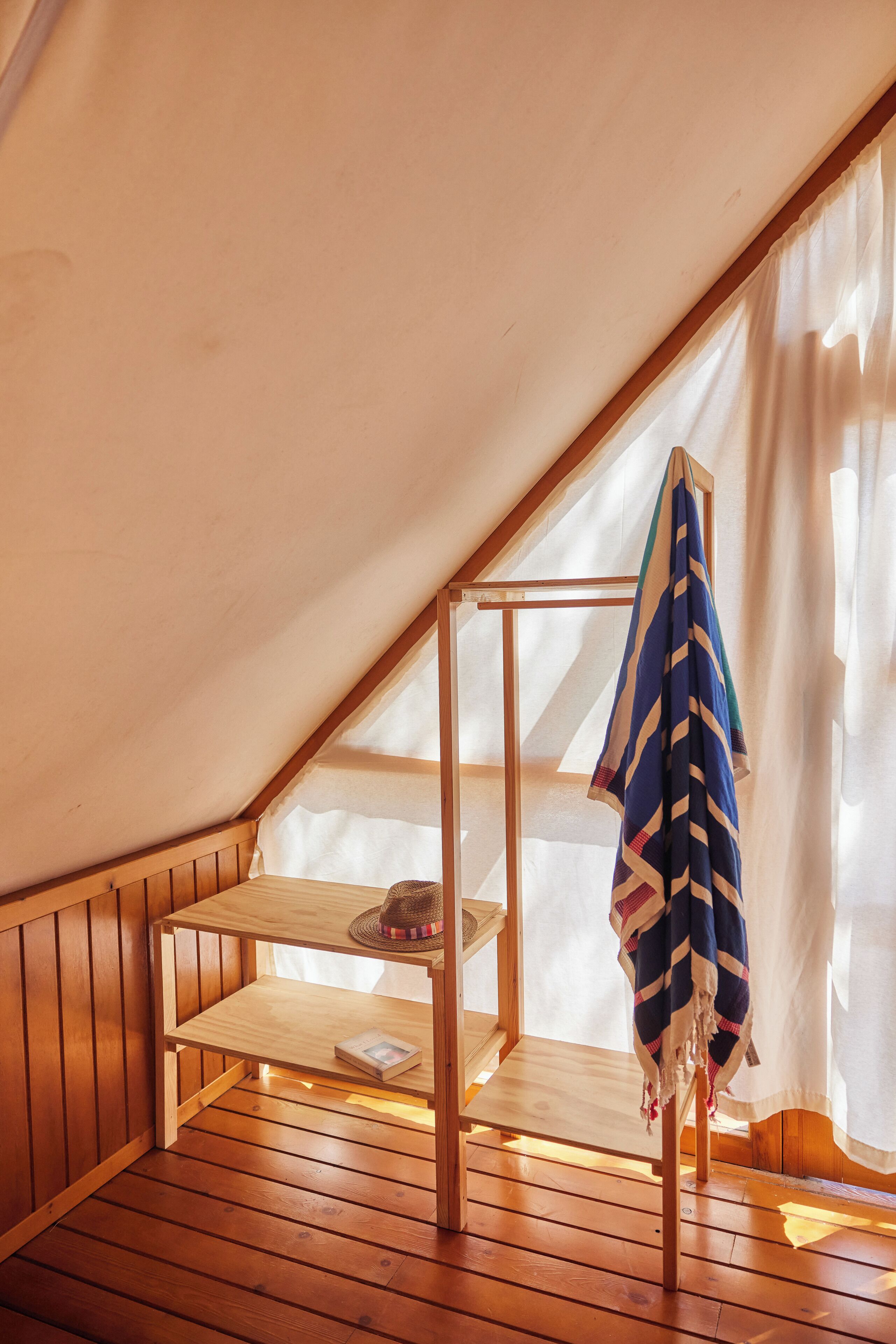 Une petite pièce mansardée avec un plancher en bois, une étagère en bois et une serviette suspendue.