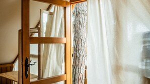 A wooden-framed window with a view of a tree trunk and a white curtain. - TAIGA Conil (Conil de la Frontera)