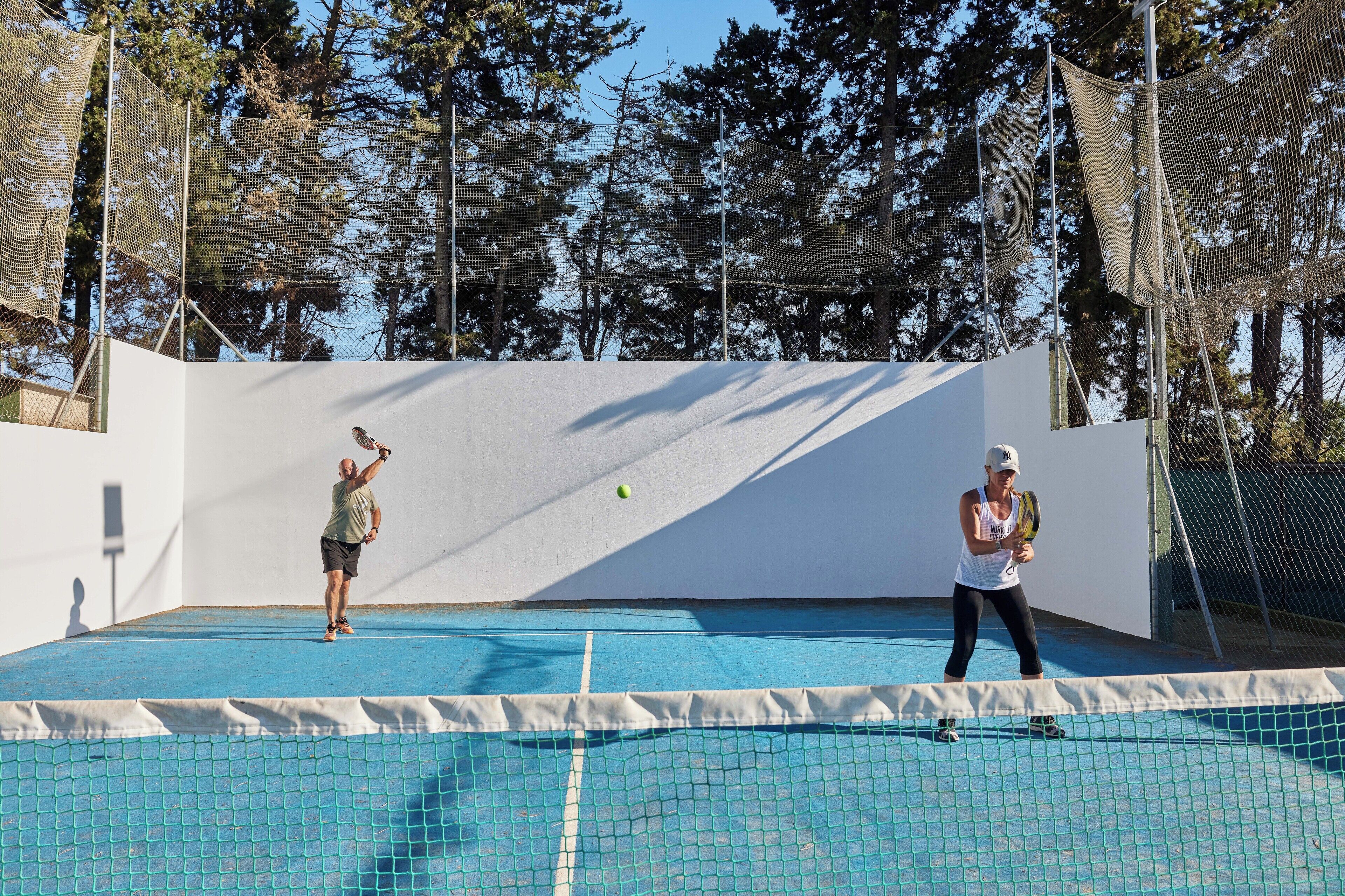 Un court de tennis en plein air, délimité par un filet et avec des arbres en arrière-plan.
