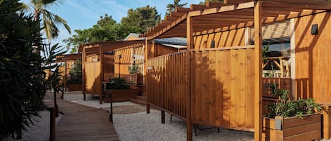 Una cabaña de madera con terraza, rodeada de grava y vegetación.