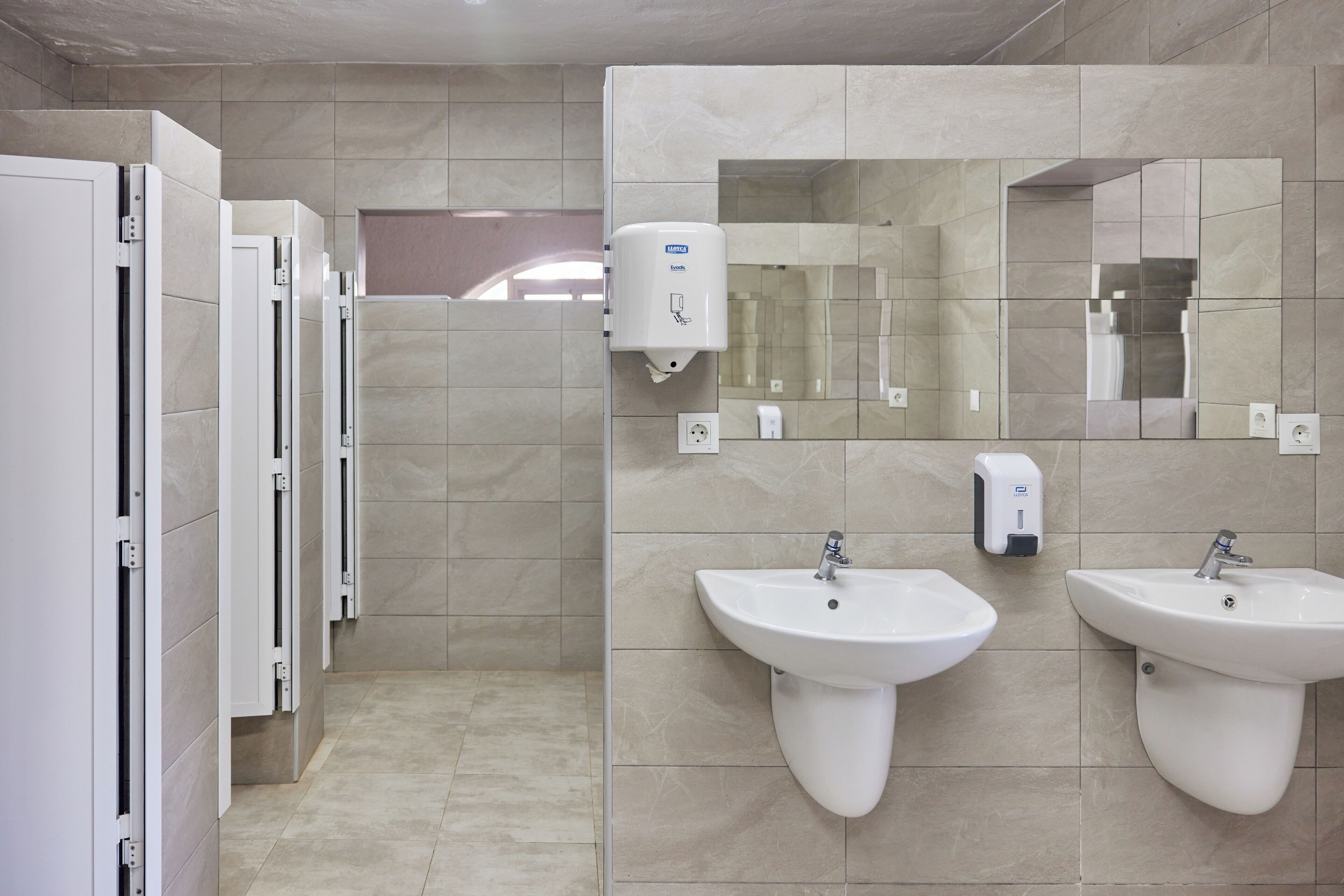 A restroom with two sinks, a hand sanitizer dispenser, and a mirror.