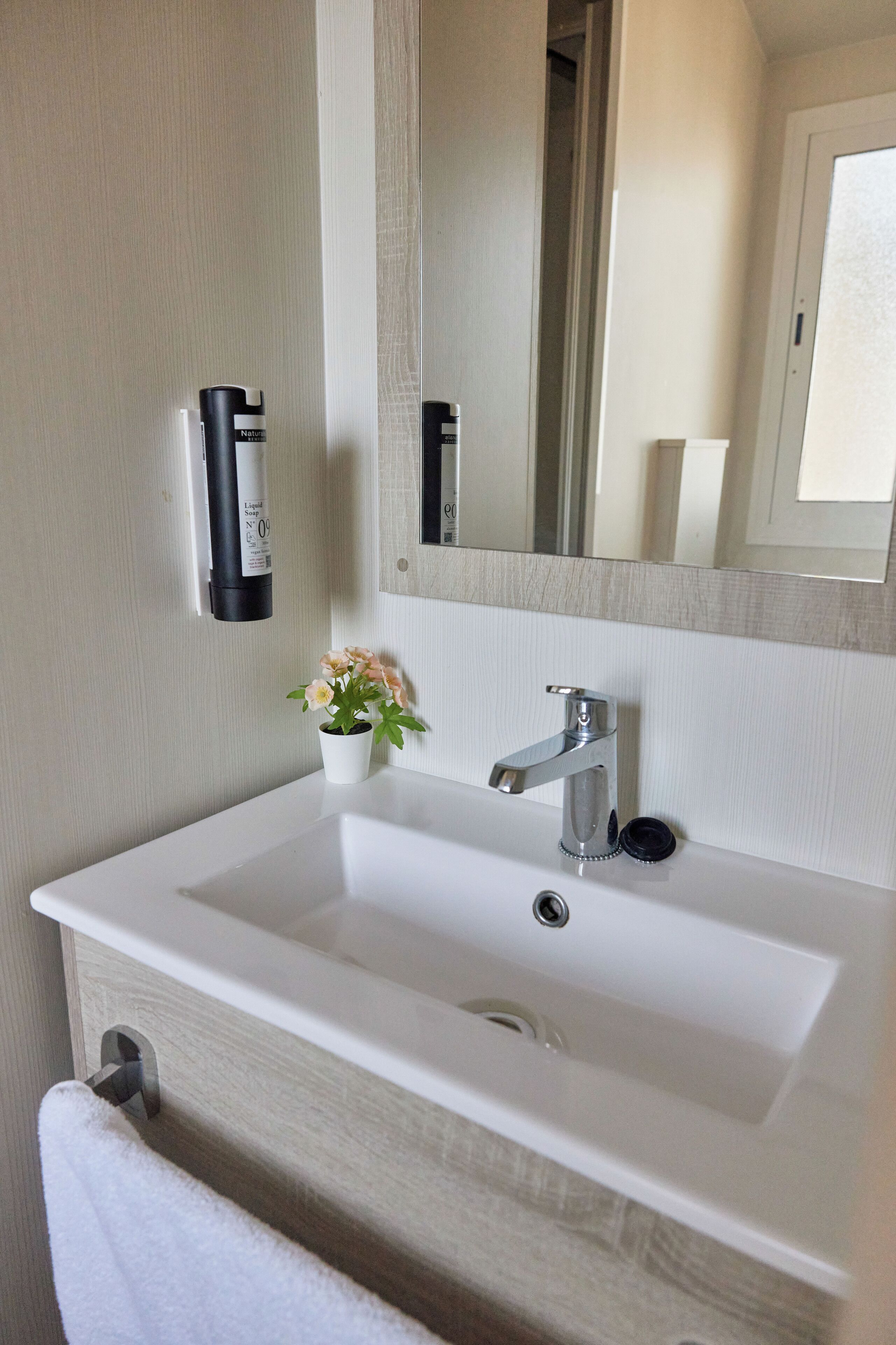 Un baño con lavamanos blanco, un espejo, toallero y una pequeña planta en maceta.