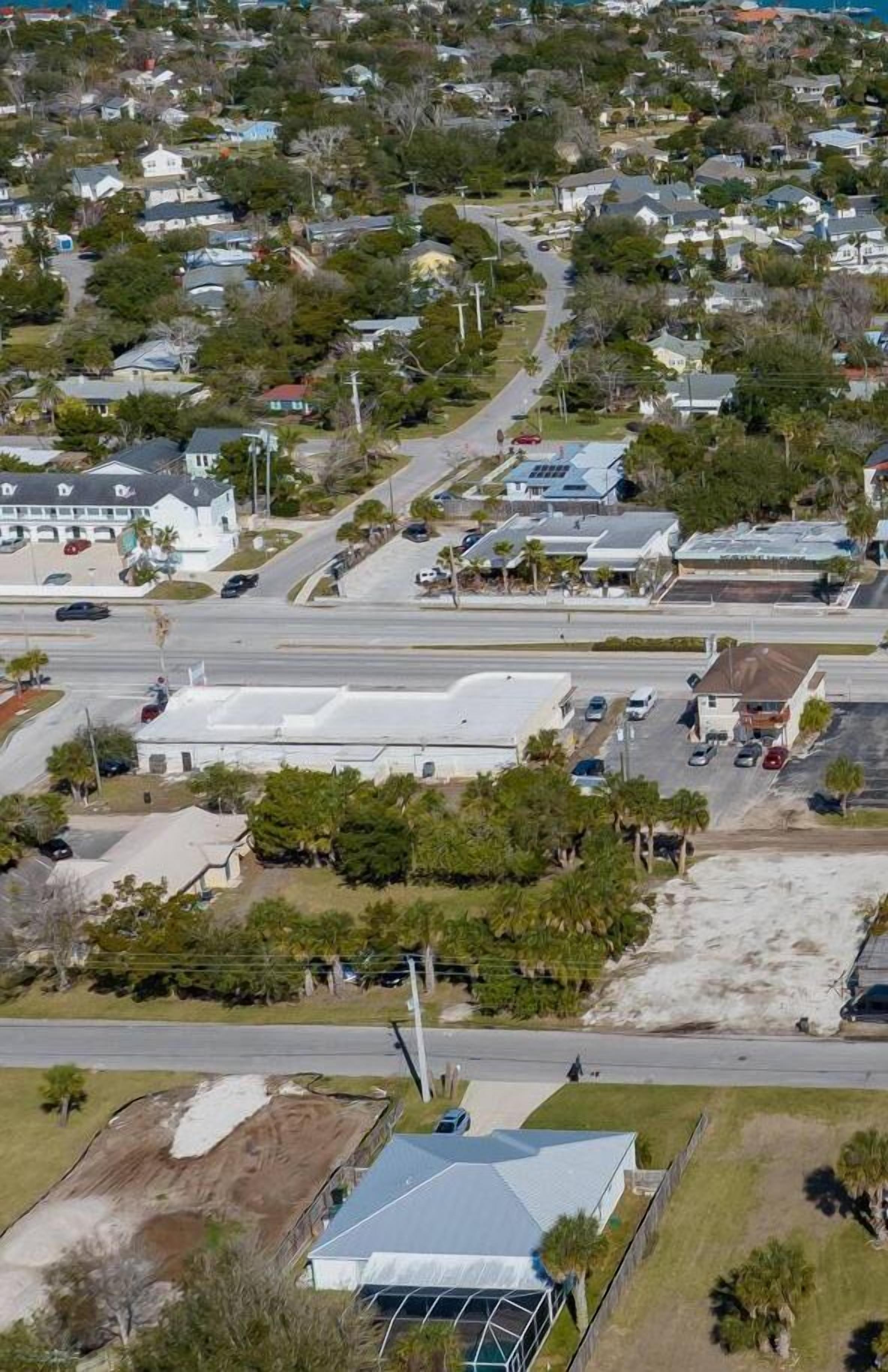 An aerial view of a residential area with houses, roads, and a large building with a white roof.