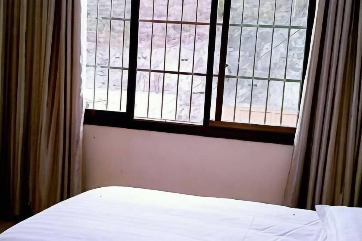 A room with a bed, a window with metal bars, and curtains.
