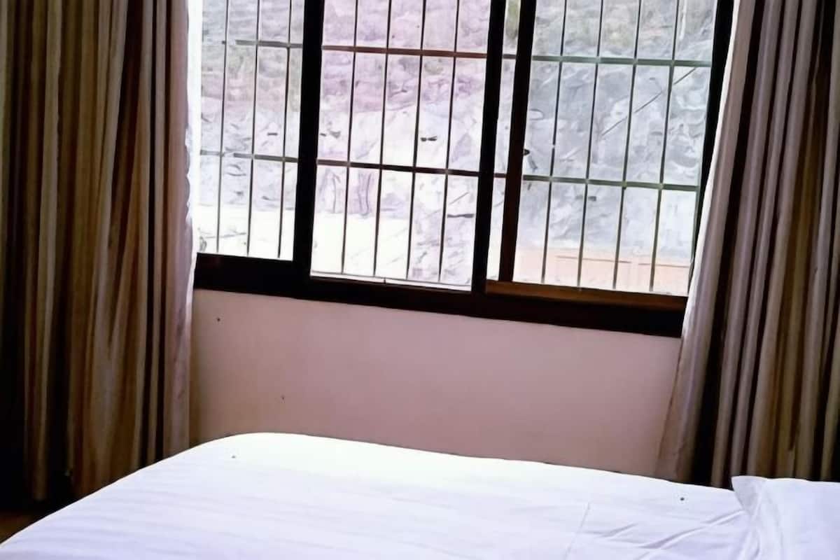 Una habitación con cama, ventana con barrotes y cortinas.