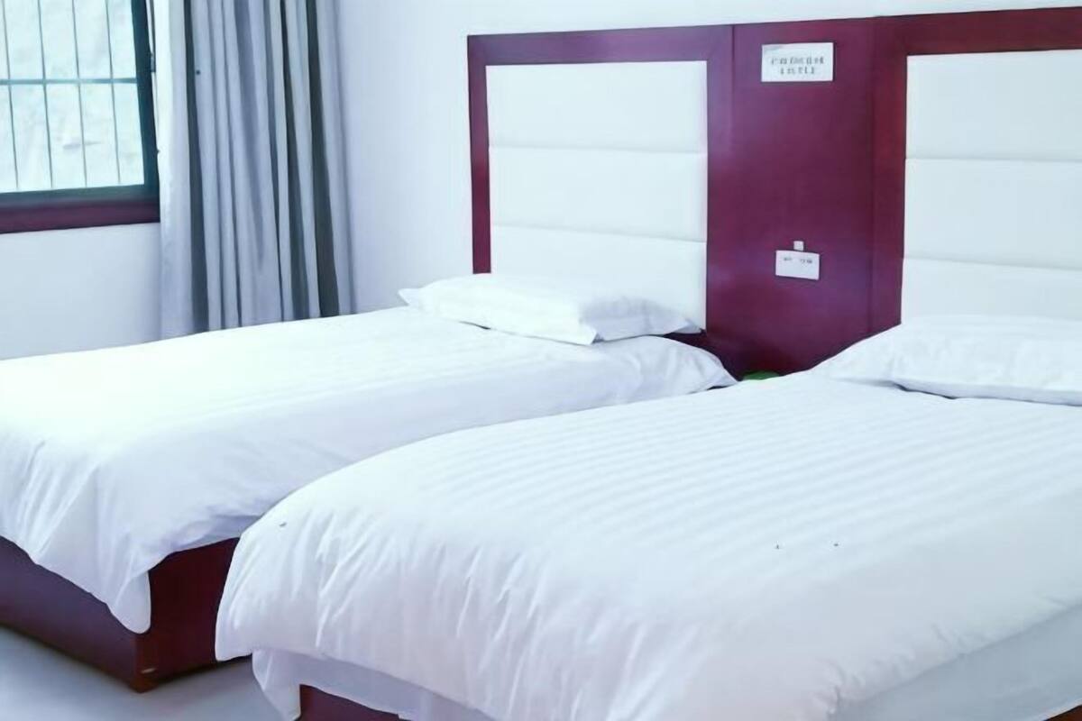 Two single beds with white linens, a wooden headboard, and a window with curtains.