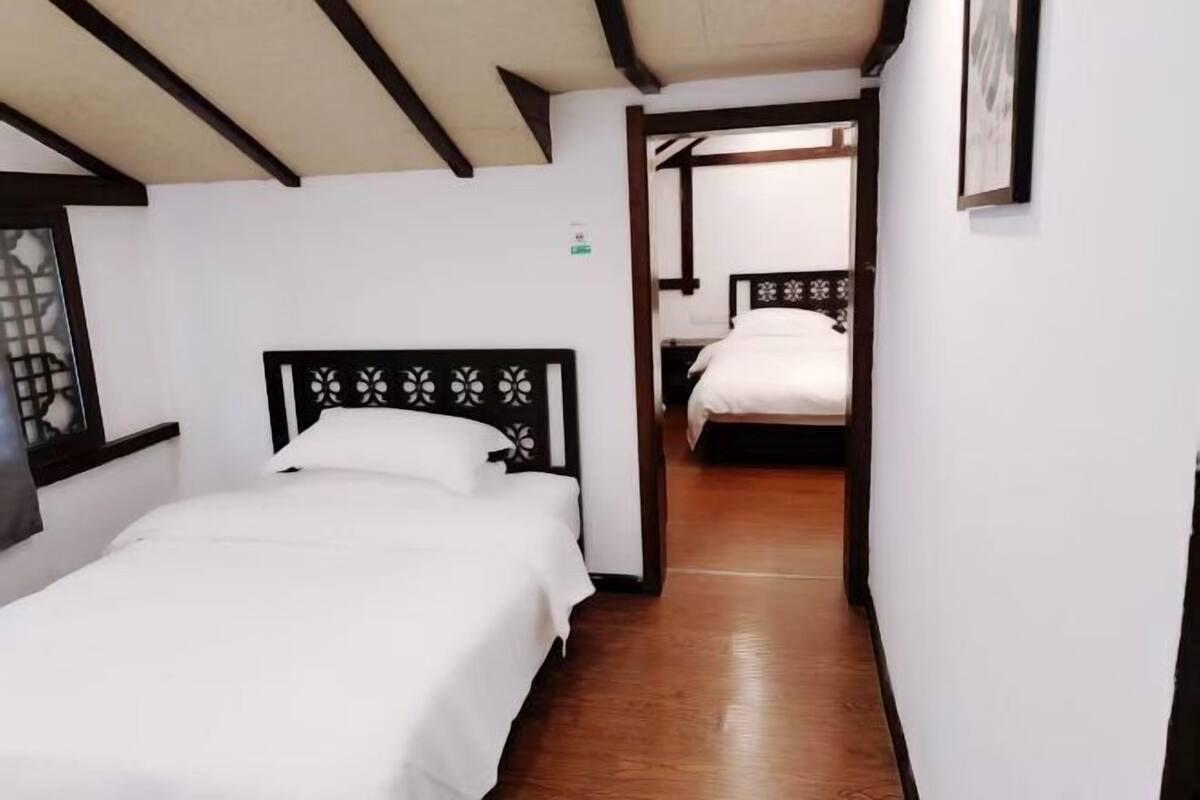 Une chambre d’hôtel avec un plancher en bois, un lit doté d’une tête de lit noire et une porte donnant sur une autre pièce.