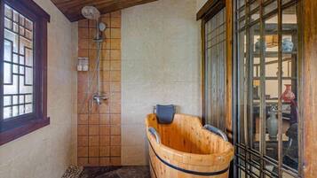 Una habitación de estilo japonés tradicional con una bañera de madera, zona de ducha y un ventanal con vistas al exterior.