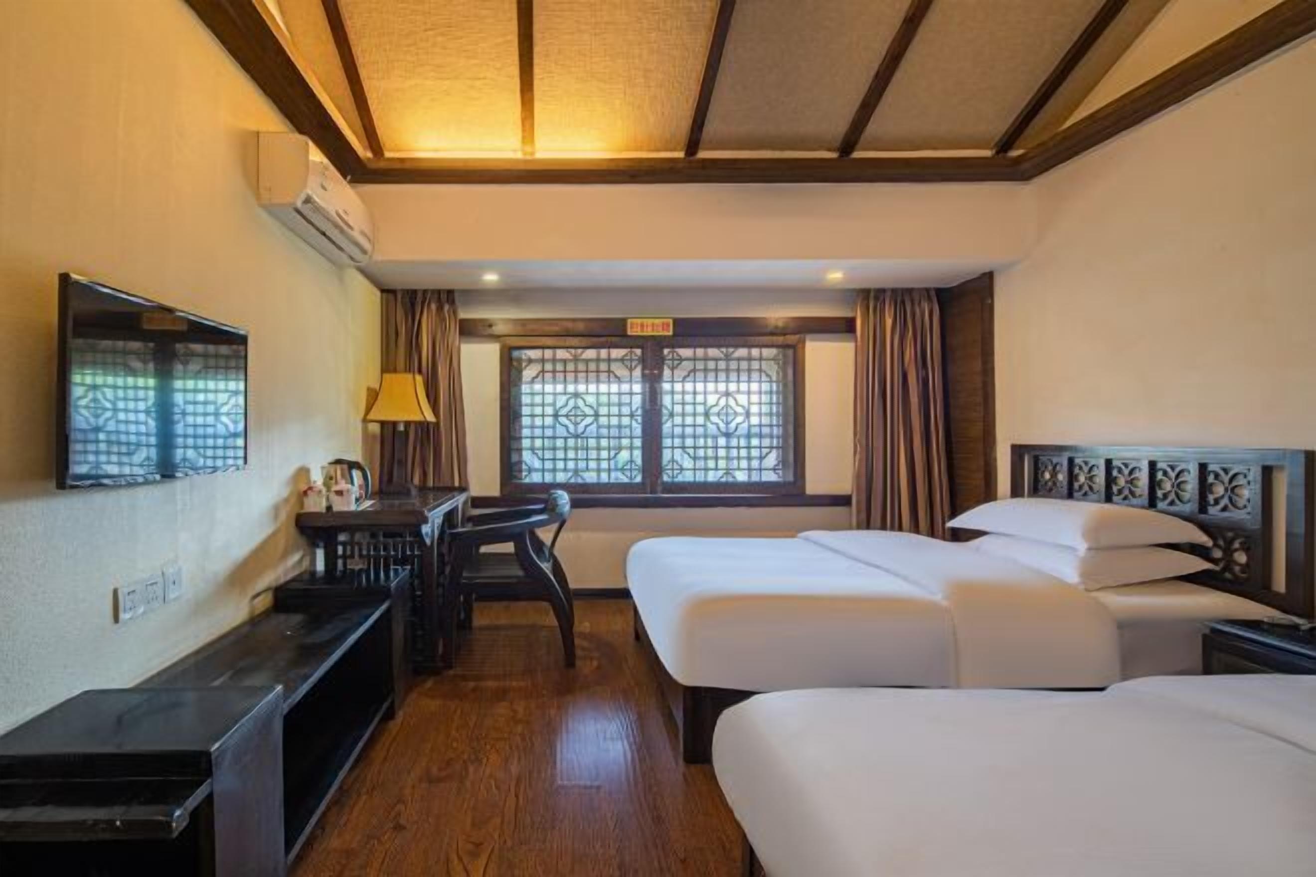 Una habitación de hotel con dos camas, un escritorio, un televisor y una ventana con cortinas.