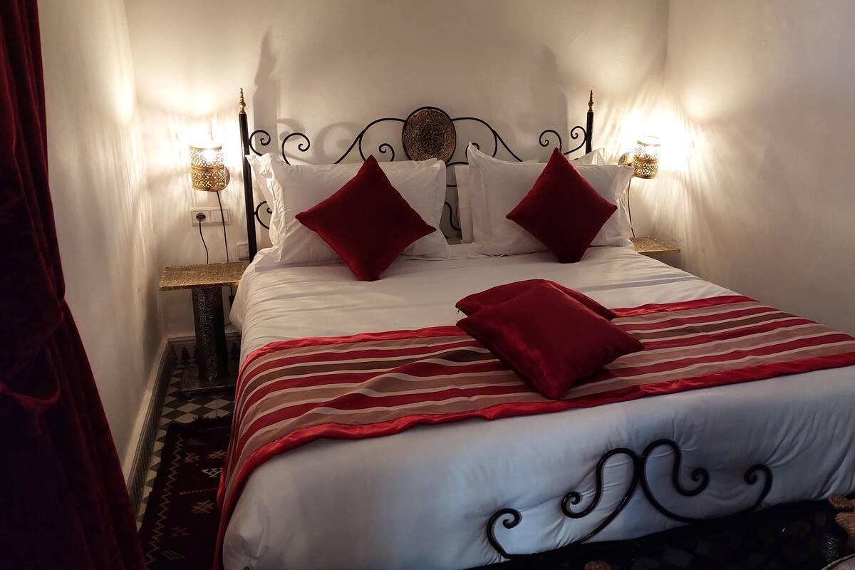 A neatly made bed with white and red bedding, two decorative pillows, and a striped blanket.