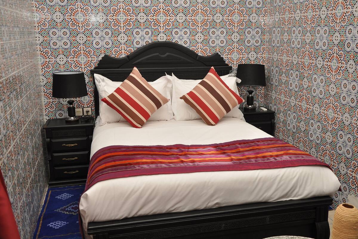 A neatly made bed with striped pillows, a black headboard, and a patterned wall.