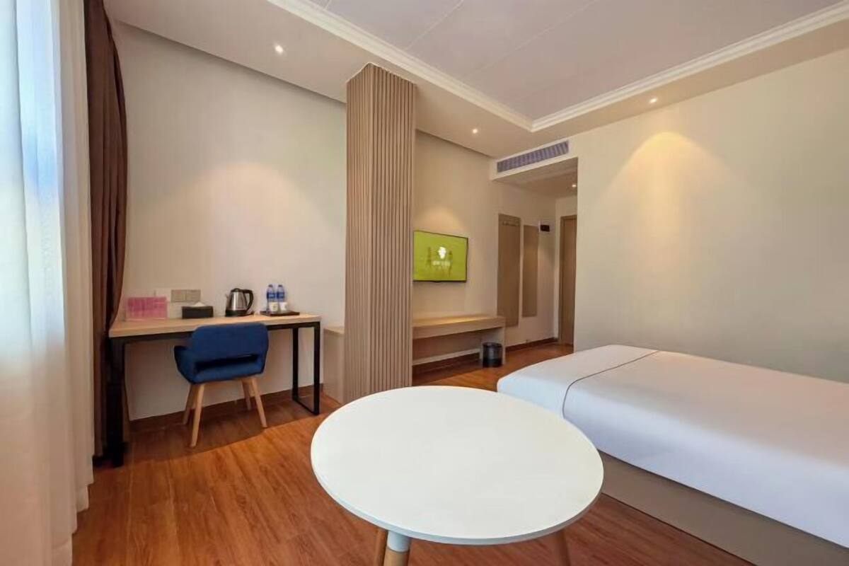 A hotel room with a bed, a desk with a chair, a round table, and a TV on the wall.