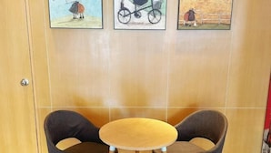 Ein Zimmer mit zwei dunkelbraunen Sesseln und einem kleinen Holztisch. Darüber an der Wand befinden sich drei gerahmte Kunstwerke.