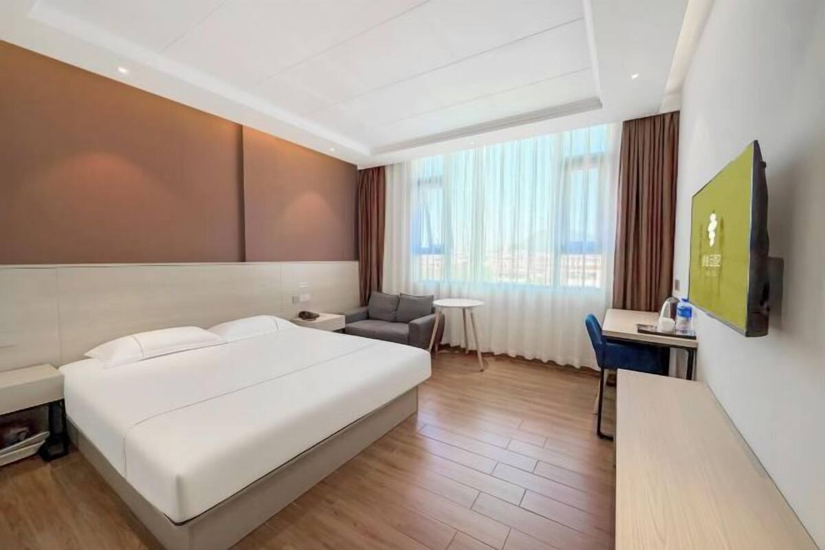 A hotel room with a bed, a desk, a chair, a small table, and a TV on the wall.