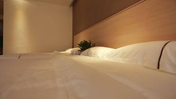 A hotel room with a neatly made bed, a wooden headboard, and a small plant on the nightstand.