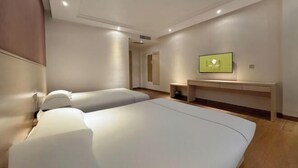 Ein modernes Hotelzimmer mit zwei Betten, einem Flachbildfernseher, einem kleinen Schreibtisch und einem begehbaren Kleiderschrank.
