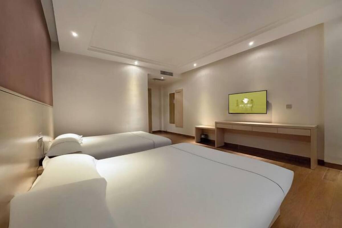 A modern hotel room with two beds, a flat-screen TV, a small desk, and a walk-in closet.