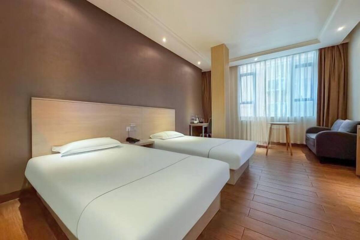 A hotel room with two beds, a desk, a chair, and a sofa.