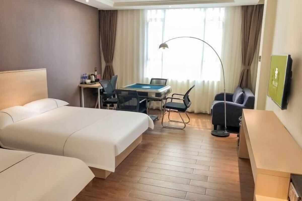 A hotel room with a bed, a desk with a chair, a lamp, and a TV.