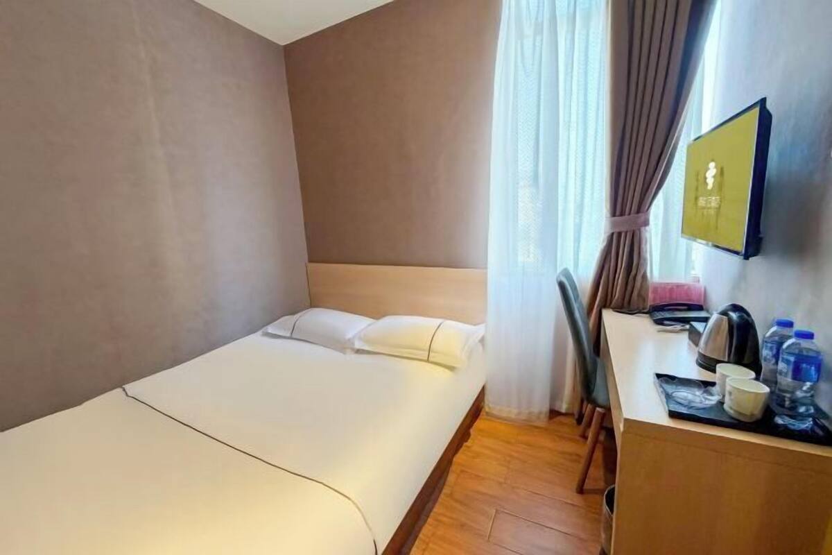 A hotel room with a bed, a desk with a chair, a television, and a window with curtains.