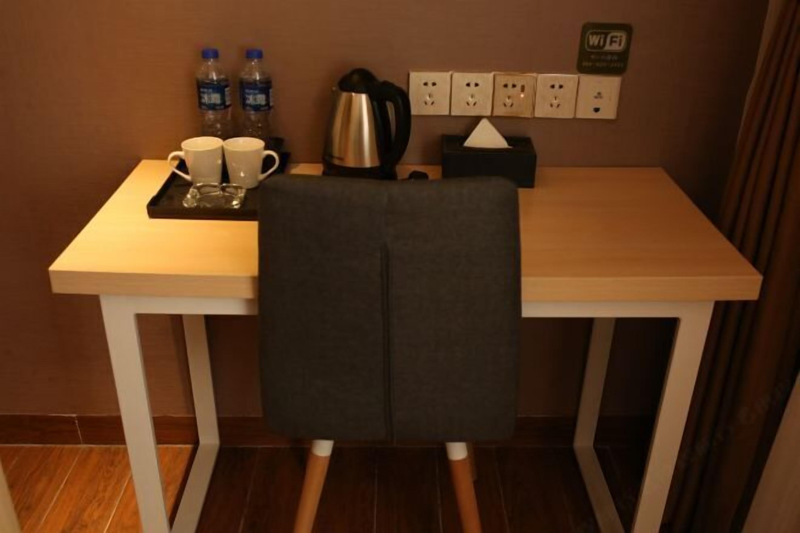 A small room with a desk, a chair, a kettle, two water bottles, and a Wi-Fi sign on the wall.