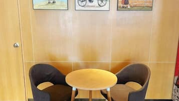 A room with a wooden door, two chairs around a small round table, and three framed pictures on the wall.