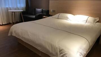 A hotel room with a large bed, a small round table, a sofa, and a window with curtains.