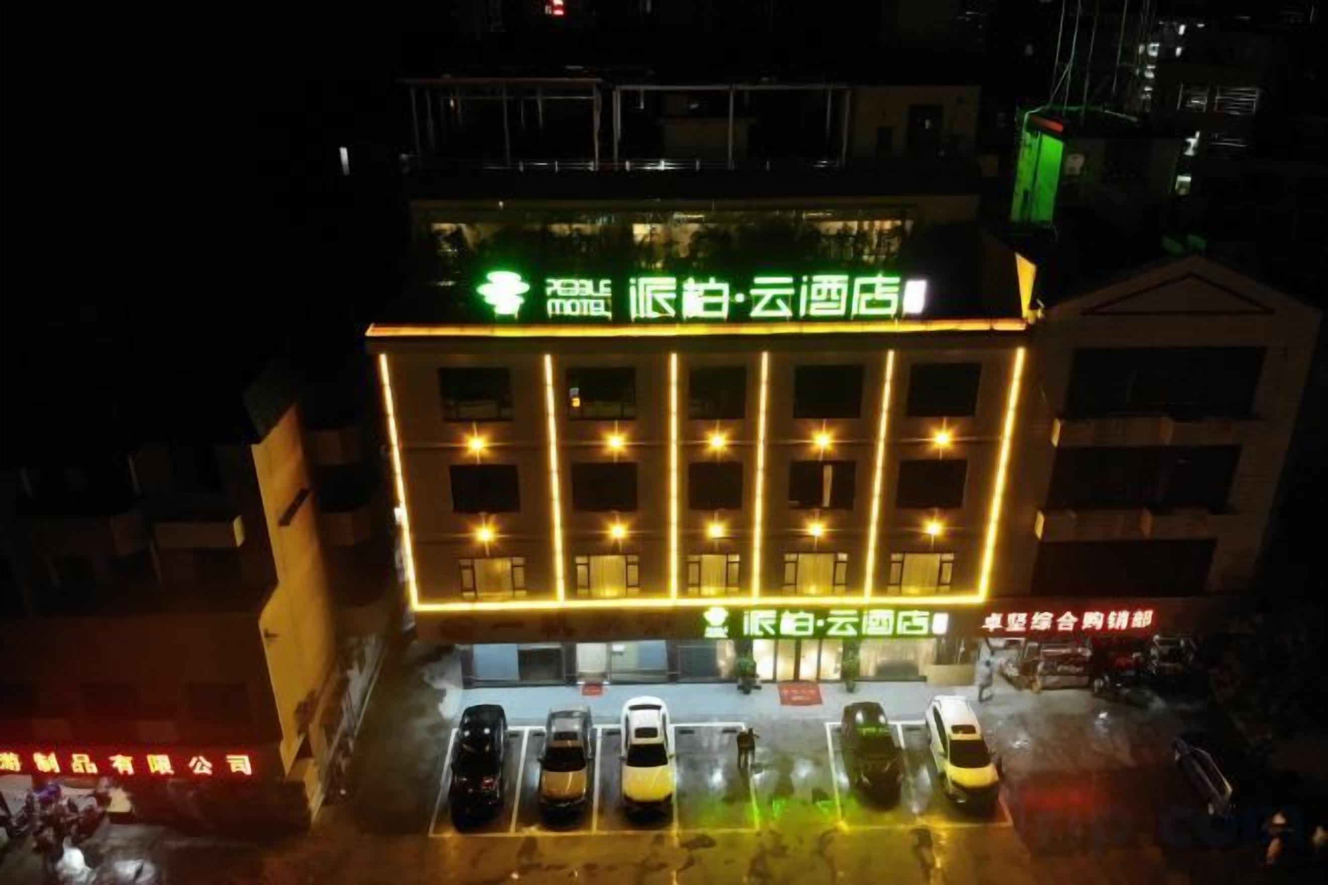 Entrada de hotel con un letrero, varios coches estacionados frente a ella y un edificio con ventanas iluminadas.