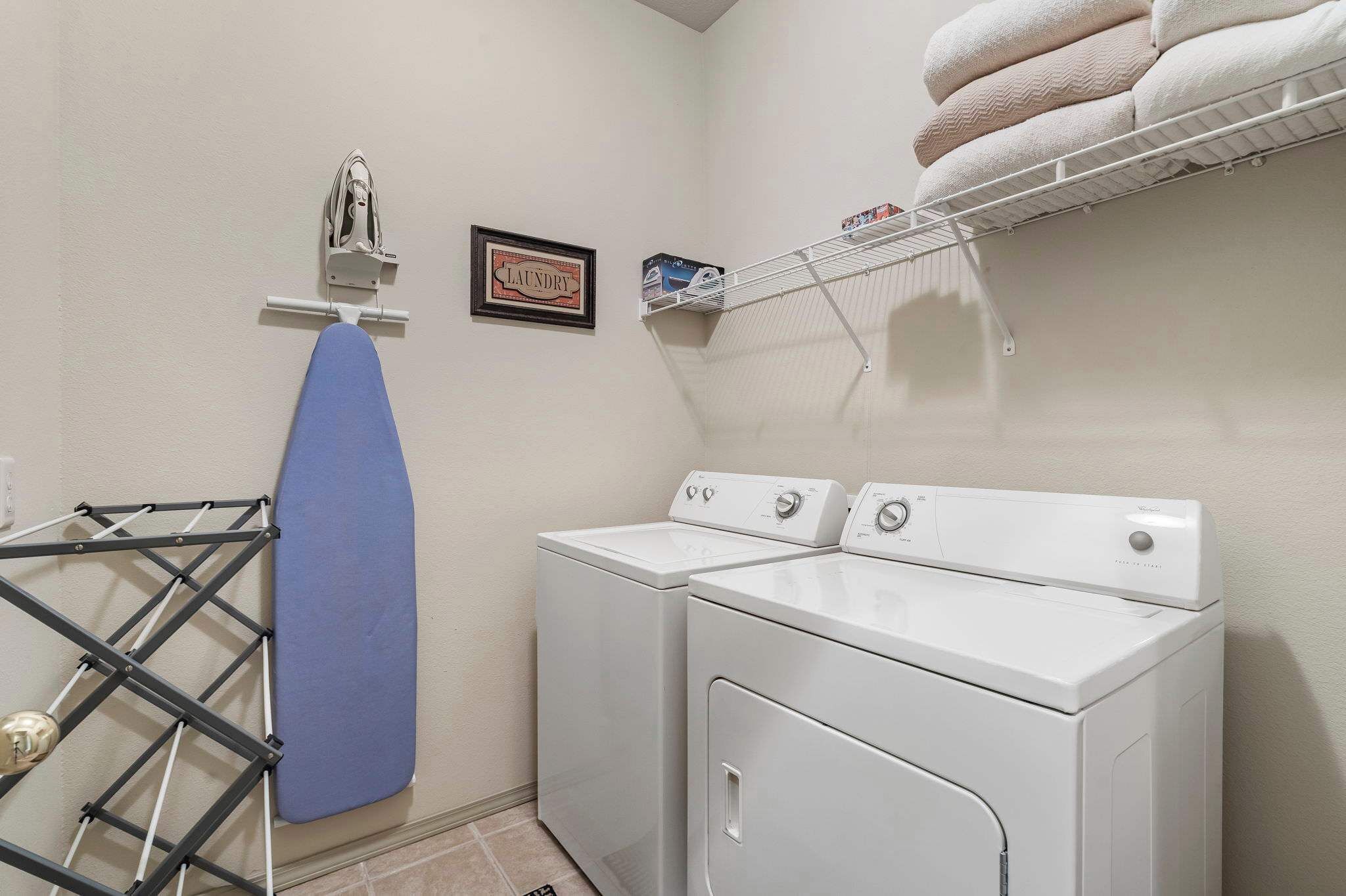 A laundry area with two white washers and dryers, a drying rack, and a laundry sign on the wall.